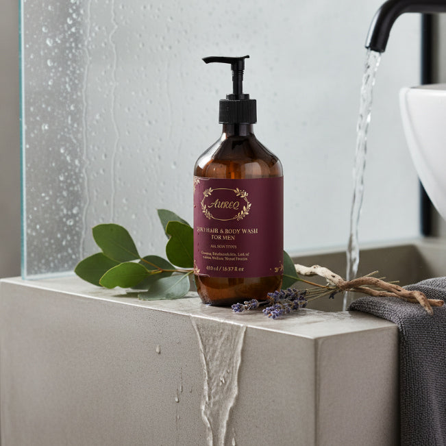 Bottle of Auroz hair and body wash for men on a bathroom counter with water flowing from a faucet.